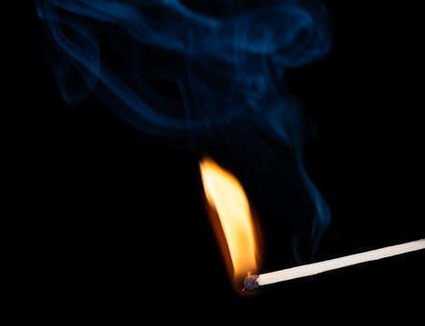Burning wooden match with smoke over black background. Copy space