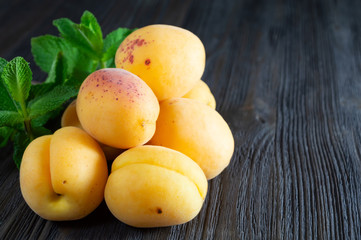 Fresh apricots and mint leaves on dark wooden background.