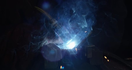 4K Extreme close up of white hot flames & smoke & sparks in metalwork shop. Slow motion