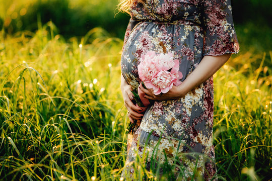 pregnant woman holding her belly and flower in the garden.