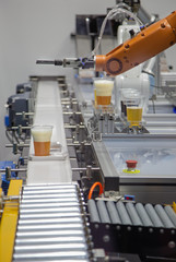 Robot pouring beer to a glass and serve on conveyor. Industrial technology