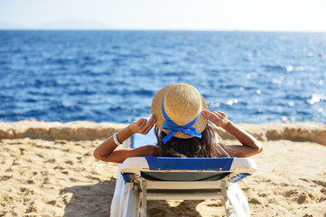 Beautiful woman sunbathing on a beach at tropical travel resort, enjoying summer holidays. Young woman lying on sun lounger near the sea. Happy serene woman