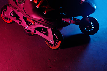 Close up view of roller skates inline skate or rollerblading on dark grunge background in neon blue magenta pink light