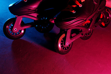 Close up view of roller skates inline skate or rollerblading on dark grunge background in neon blue magenta pink light