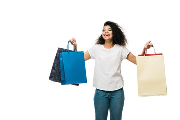 Fototapeta na wymiar positive african american girl holding shopping bags while standing isolated on white