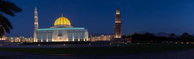Obraz premium A Panorama of the Sultan Qaboos Grand Mosque in Muscat, Oman in the early evening hour showing off the dark blue sky and glowing dome. 