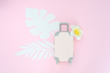 Pink travel suitcase on pink background with tropical leaves and white flower. Concept for travel. Flat lay exotic