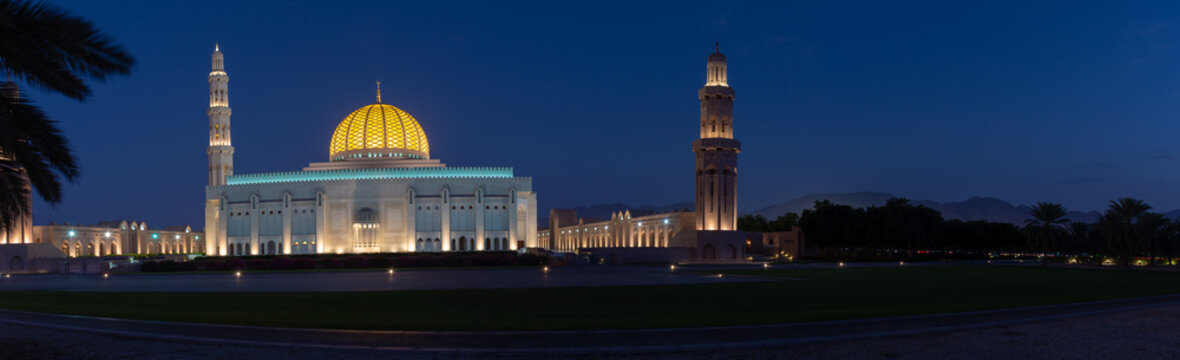 A Panorama of the Sultan Qaboos Grand Mosque in Muscat, Oman in the early evening hour showing off the dark blue sky and glowing dome. 