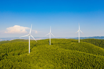 Parco eolico con turbine da 100 metri di diametro per la produzione di energia verde dal vento, su una collina con alberi. Vista aerea con drone.