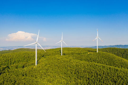 Parco eolico con turbine da 100 metri di diametro per la produzione di energia verde dal vento, su una collina con alberi. Vista aerea con drone.