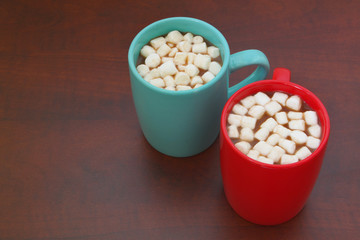 Red and blue cups with cocoa drink and marshmallows on wooden table with room for text