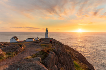 Beautiful sunrise over a white lighthouse sitting at the edge of a rocky cliff. Cape Spear National...