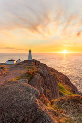 Beautiful sunrise over a white lighthouse sitting at the edge of a rocky cliff. Cape Spear National...