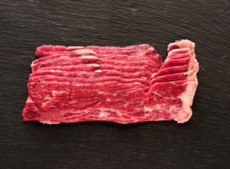 Raw marbled beef slices on a black slate background, top view