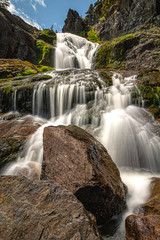 Fototapeta premium Smooth flowing waterfall cascading down rocks with vibrant green moss growing on them. Flatrock falls, Newfoundland. 