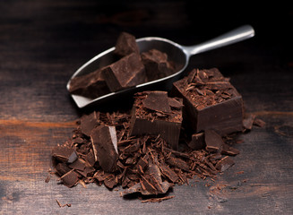 Pieces  dark chocolate on a wooden background and metal scoop