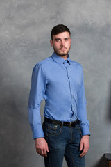Handsome young stylish man standing in blue shirt in interior on gray background