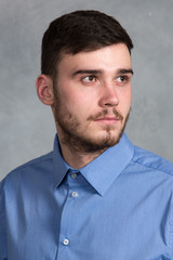 Handsome young stylish man standing in blue shirt in interior on gray background