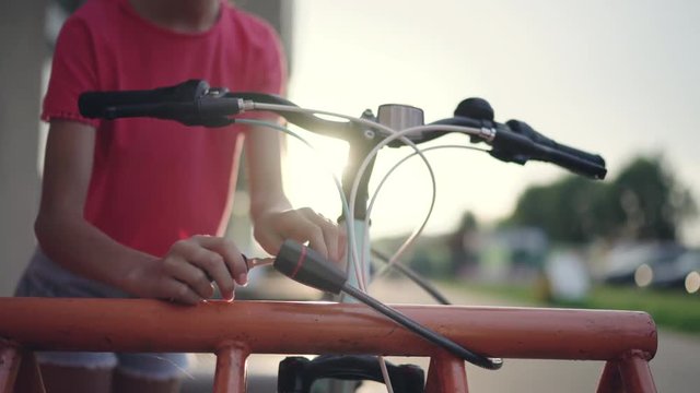 Girl teenager unlock her bicycle on street parking. Sunset time