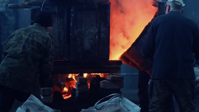 View of men in protective coveralls on the old steel making plant working with melting furnace. Stock footage. Industrial details of metallurgic factory