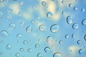 Water drops on glass window over blue sky. Water drops background.