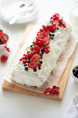 Sponge (biscuit) cake roll filling whipped cream and berries decorated strawberry, blueberry and red currants on white wooden background. Soft focus. Summer food concept