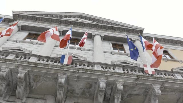The consulate house with country flags waving in the wind, bottom view. Action. Vintage architecture with modern flying flags on the building.