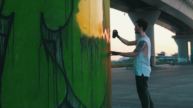 Man with spray bottle drawing graffity under the bridge at the suny day