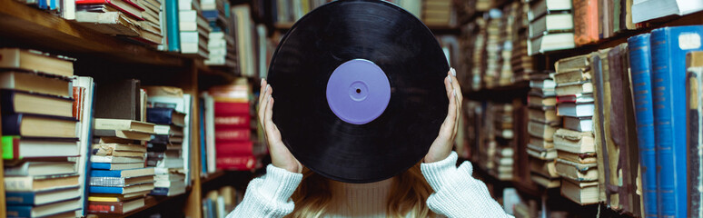 panoramic shot of young adult woman holding vinyl in library