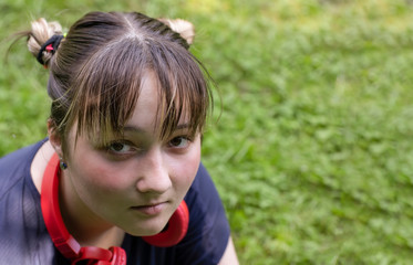 Portrait of a teenage girl sitting on the grass in a city park in a blue t-shirt and jeans with red headphones.