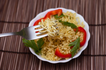 Instant noodles with red sweet peppers and greens in a white bowl. Appetizing Egg Noodles