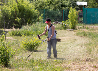 A man mows the grass with a gasoline trimmer.