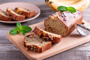 Banana bread with bananas sliced on a wooden cutting board with bananas in background