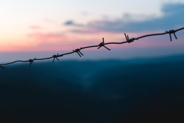 Barbed wire on the background of the sunrise in the mountains. Early morning purple blue