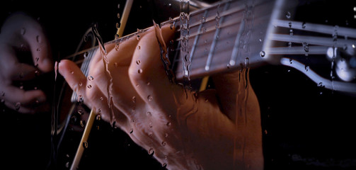 musician playing guitar at studio behind the glass with water drops