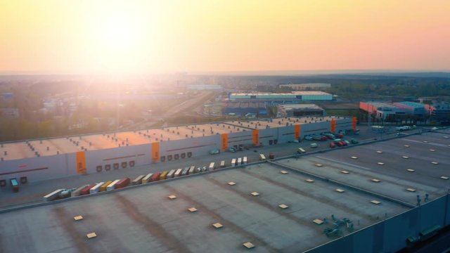 Aerial side view of logistics park with warehouse, loading hub with many semi-trailers trucks standing at the ramps for load/unload goods at sunset