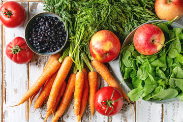 Variety of fresh fruits, vegetables and berries carrot, spinach, tomatoes, red apples, blueberries over white plank wooden background. Flat lay, space