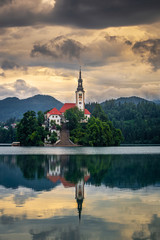 Fototapeta na wymiar Bled, Slovenia - Golden sunrise at Lake Bled (Blejsko Jezero) with the Pilgrimage Church of the Assumption of Maria on a small island and Julian Alps at background at summer time