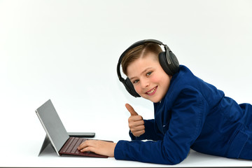 Stylish teenager boy with headphones and mobile phone laptop laying on a floor. Cute boy with headphones listens to the music. Schoolboy plays games on laptop isolated over white background.