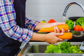 Young woman washing carrot to remove pesticides before cooking in kitchen. Fruit and vegetables washing concept.