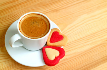Cup of hot coffee with a pair of heart shaped cookies on wooden table with copy space