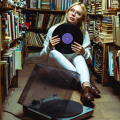 beautiful and blonde woman sitting on floor and holding vinyl in library