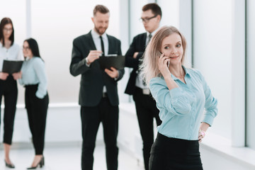 young business woman talking on a smartphone standing in the office hallway.