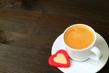 One cup of hot espresso coffee with a heart shaped cookie on dark brown wooden table with copy space
