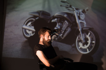 Plakat serious stylish biker man looking through the slides of his motorcycle