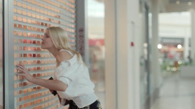 Young blonde woman knocking on the door of a closed clothing store. Close-up of embarassed girl shopoholic addictive trying to open the shop to buy new clothes.
