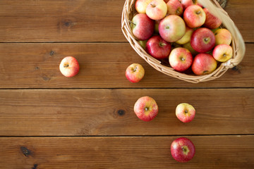 fruits, food and harvest concept - ripe apples in wicker basket on wooden table