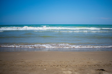 Fototapeta na wymiar Mar azul turqueza en calma, con olas pequeñas y cielo azul despejado, con arena dorada