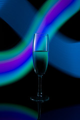 A single wine glass isolated on a black background with red white pink and orange neon light painting streaks of light behind them. Light wave, game of colors, drawing light.