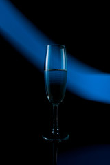 A single wine glass isolated on a black background with red white pink and orange neon light painting streaks of light behind them. Light wave, game of colors, drawing light.